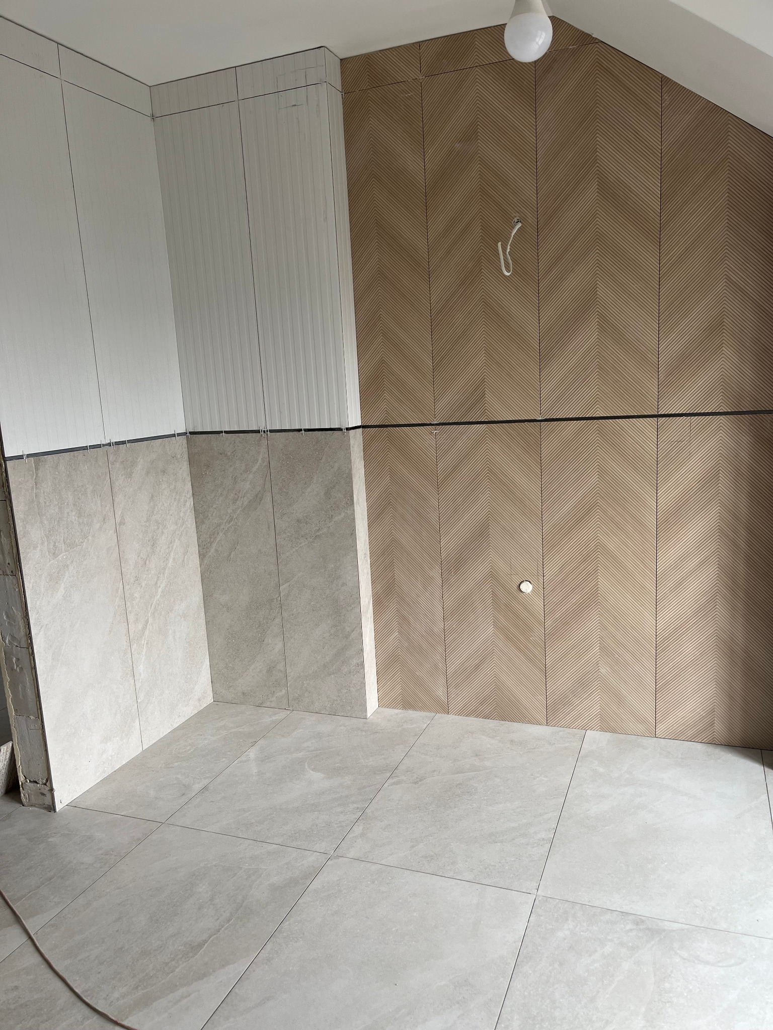 Wnętrze w trakcie wykańczania: częściowo ułożone płytki podłogowe i ścienne, w tym dekoracyjna ściana z wzorem jodełki. Widoczne elementy instalacji.