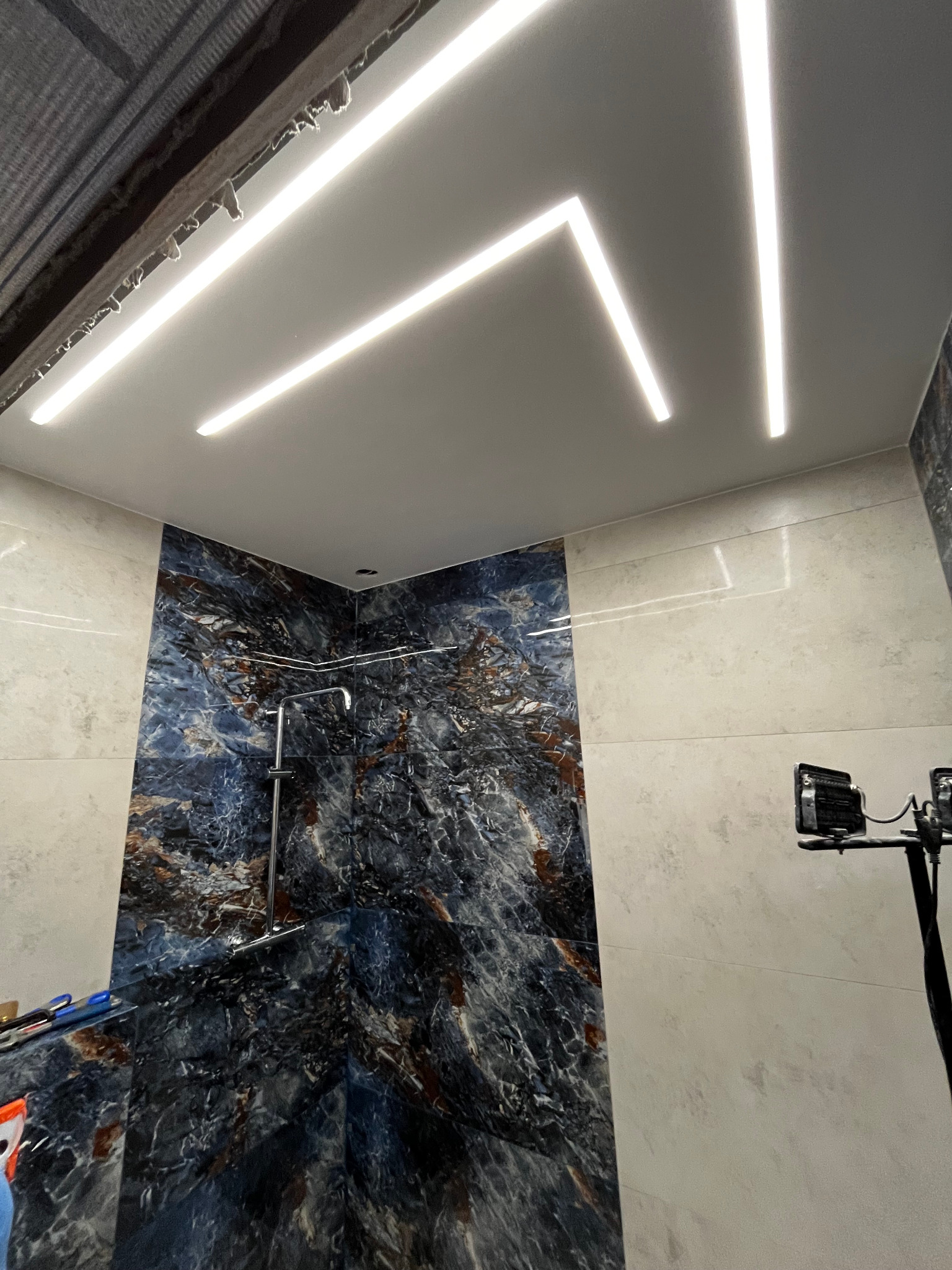 Nowoczesna łazienka z marmurowymi płytkami w odcieniach błękitu i beżu, oświetlona liniowymi lampami LED w suficie, widok z dołu.