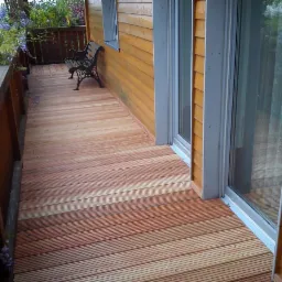 Drewniany taras z desek kompozytowych, z widokiem na ogród i ławką z kutego żelaza.