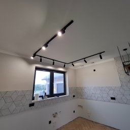HOUSE-Technic Usługi Ogólnobudowlane - Jasna kuchnia w trakcie wykańczania: heksagonalne płytki, parkiet w jodełkę, czarne szyny z reflektorami. Widoczne przygotowane punkty elektryczne.