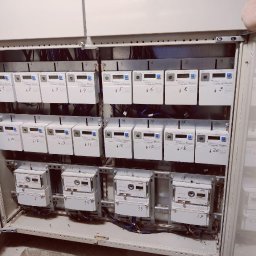 EURO-INWEST SPÓŁKA Z OGRANICZONĄ ODPOWIEDZIALNOŚCIĄ - Rozdzielnia elektryczna z wieloma licznikami energii, każdy oznaczony numerem. Widoczne przewody i elementy montażowe wewnątrz metalowej szafy.