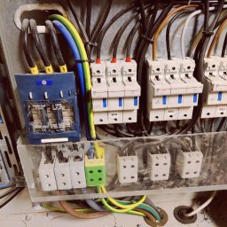 EURO-INWEST SPÓŁKA Z OGRANICZONĄ ODPOWIEDZIALNOŚCIĄ - Szczegółowe ujęcie tablicy rozdzielczej z bezpiecznikami, przewodami oznaczonymi numerami i kolorami, oraz fragmentem żółto-czerwonego śrubokręta w dolnej części kadru.