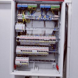 EURO-INWEST SPÓŁKA Z OGRANICZONĄ ODPOWIEDZIALNOŚCIĄ - Rozdzielnica elektryczna w białej obudowie, widoczne zabezpieczenia, kable i listwy zaciskowe. Uporządkowany układ przewodów wewnątrz skrzynki.
