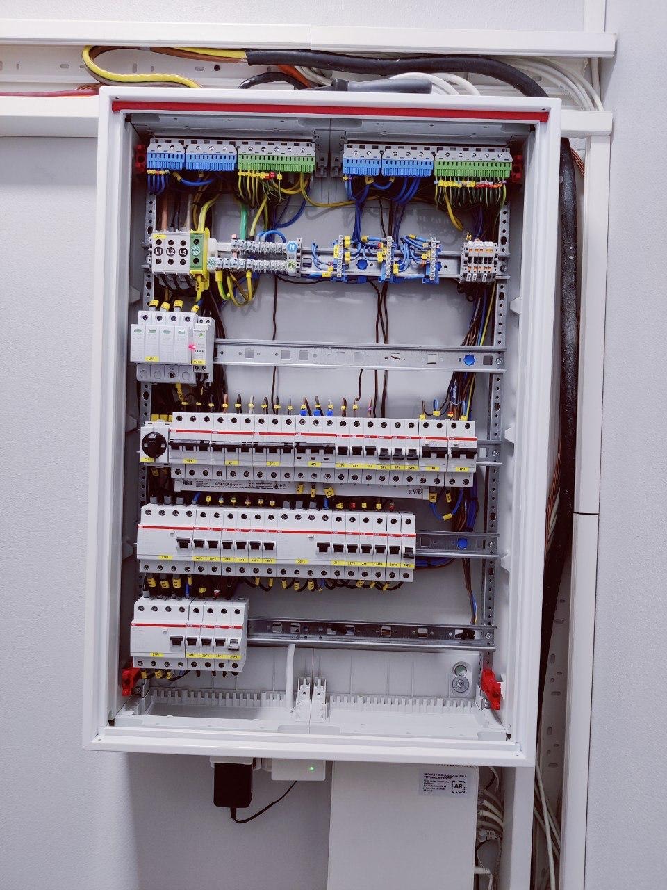 Rozdzielnica elektryczna w białej obudowie, widoczne zabezpieczenia, kable i listwy zaciskowe. Uporządkowany układ przewodów wewnątrz skrzynki.