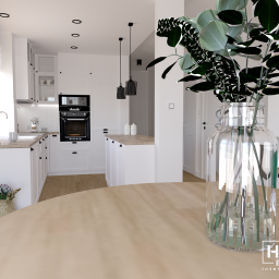 Home Effect - Jasna kuchnia z białymi szafkami i drewnianym blatem, widok z perspektywy stołu z dekoracyjnym wazonem z eukaliptusem, minimalistyczne lampy wiszące nad wyspą kuchenną.