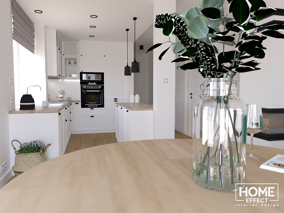 Jasna kuchnia z białymi szafkami i drewnianym blatem, widok z perspektywy stołu z dekoracyjnym wazonem z eukaliptusem, minimalistyczne lampy wiszące nad wyspą kuchenną.