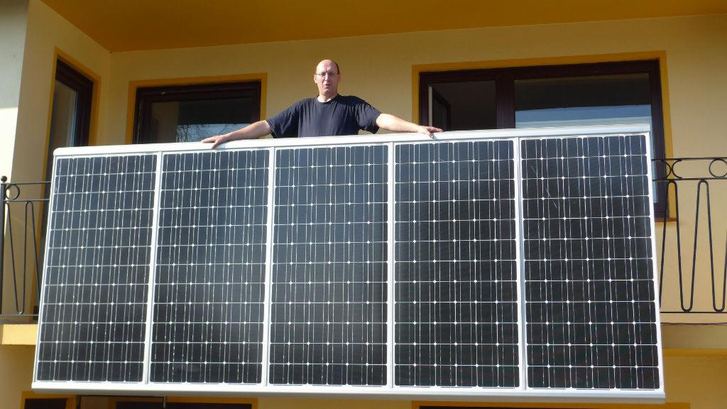 Człowiek opiera się na panelach słonecznych wystawionych na balkonie budynku o żółtej elewacji.