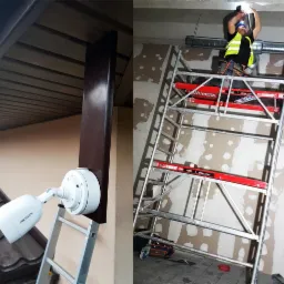 Montaż kamery monitoringu Hikvision na zewnątrz budynku, widoczny monter na rusztowaniu wewnątrz, używający latarki czołowej.