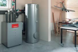 Szary piec grzewczy Viessmann z podłączonymi rurami i zasobnikiem ciepłej wody w kotłowni, w tle biurko z modelami samolotów.