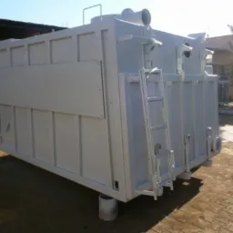 Biała, metalowa konstrukcja przemysłowa z drabinką, umieszczona na betonowych podstawach na zewnątrz, prawdopodobnie filtr lub oczyszczalnia powietrza.