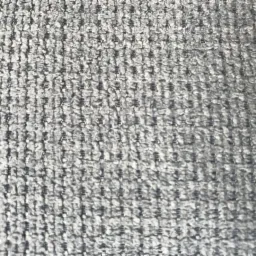 Szary materiał tekstylny o wyraźnej, regularnej strukturze i delikatnym połysku, przypominający gruby splot dywanowy lub tapicerski.