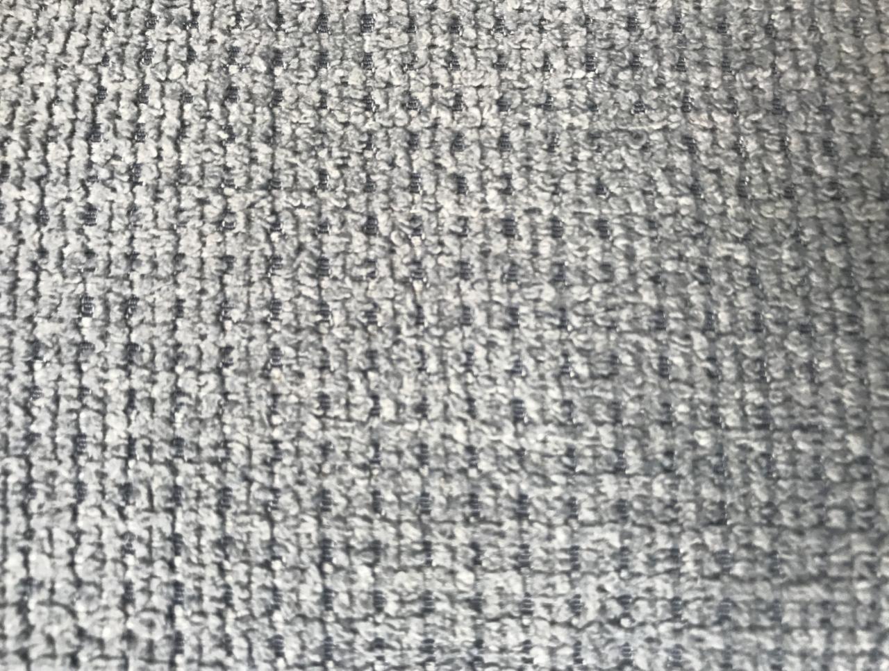 Szary materiał tekstylny o wyraźnej, regularnej strukturze i delikatnym połysku, przypominający gruby splot dywanowy lub tapicerski.