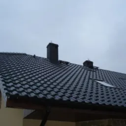 Czarny dach z dachówki ceramicznej z oknami połaciowymi i kominem w domu jednorodzinnym we Wrocławiu, sfotografowany w pochmurny dzień.