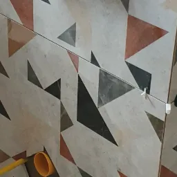 Układanie płytek z geometrycznym wzorem trójkątów, widoczne narzędzia do poziomowania i rurka odkurzacza.