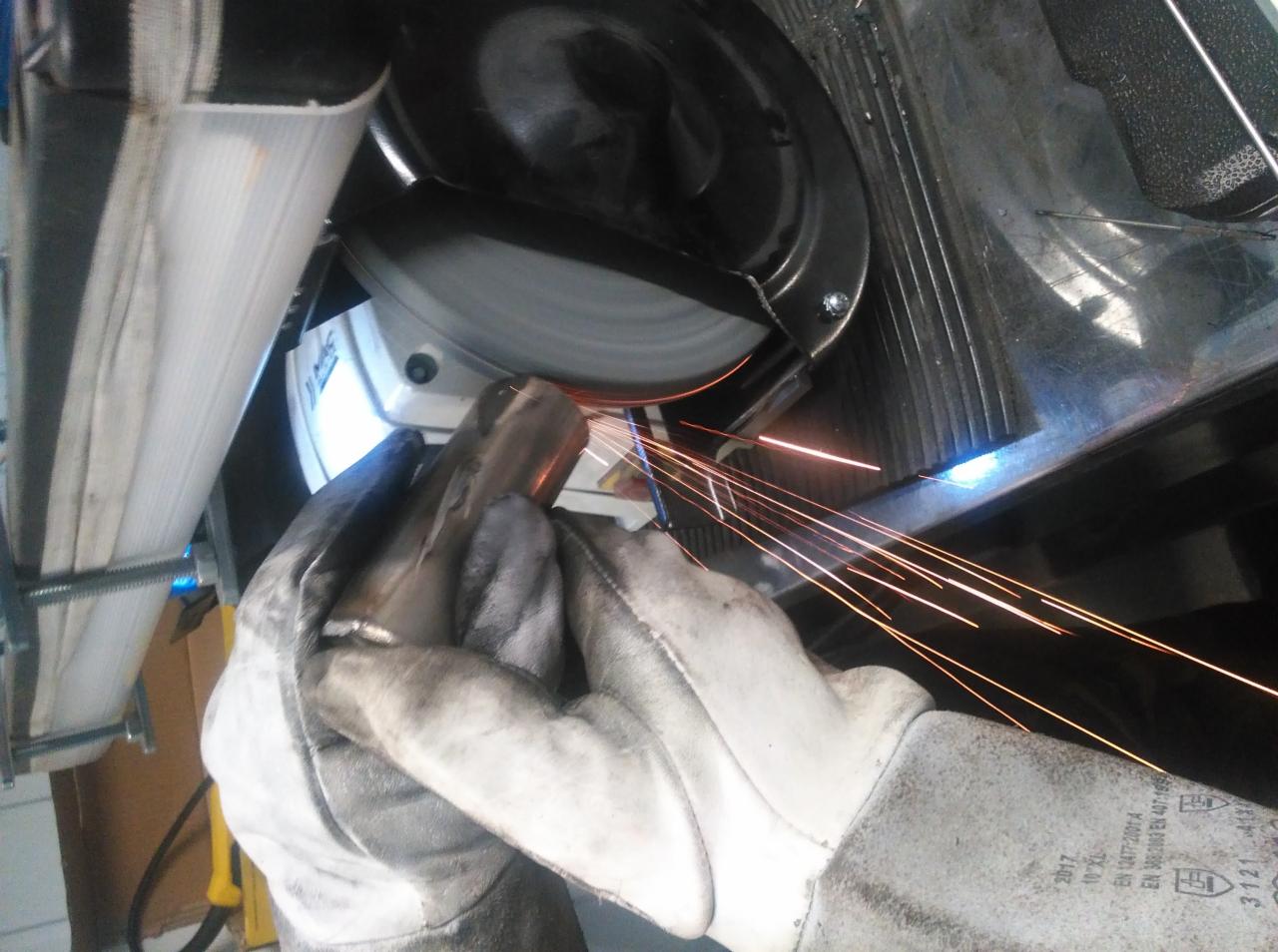Szlifowanie metalowej rury szlifierką kątową, iskry wylatują spod tarczy, ochronne rękawice robocze na dłoniach