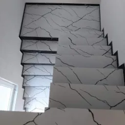 Schody wyłożone białymi płytkami z czarnym marmurkowym wzorem, czarne listwy wykończeniowe, widok z dołu na górę.