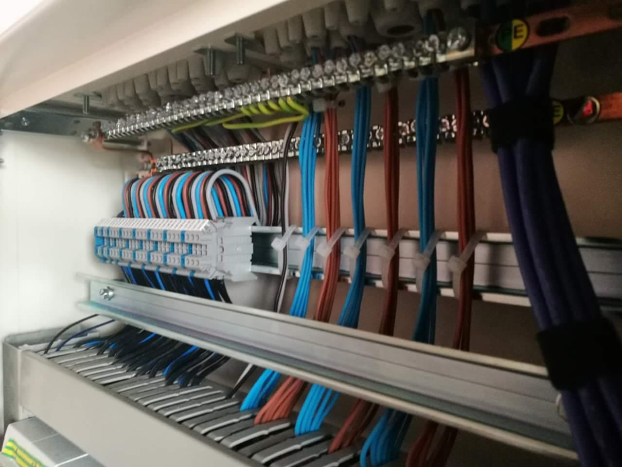 Wnętrze skrzynki rozdzielczej z uporządkowanymi przewodami w różnych kolorach, podłączonymi do listew zaciskowych i szyn montażowych.