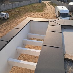 Budmar - Nowoczesna konstrukcja dachu z elementami wykończeniowymi w kolorze grafitowym, widok z góry na tle wiejskiego krajobrazu z budynkami i pojazdami.