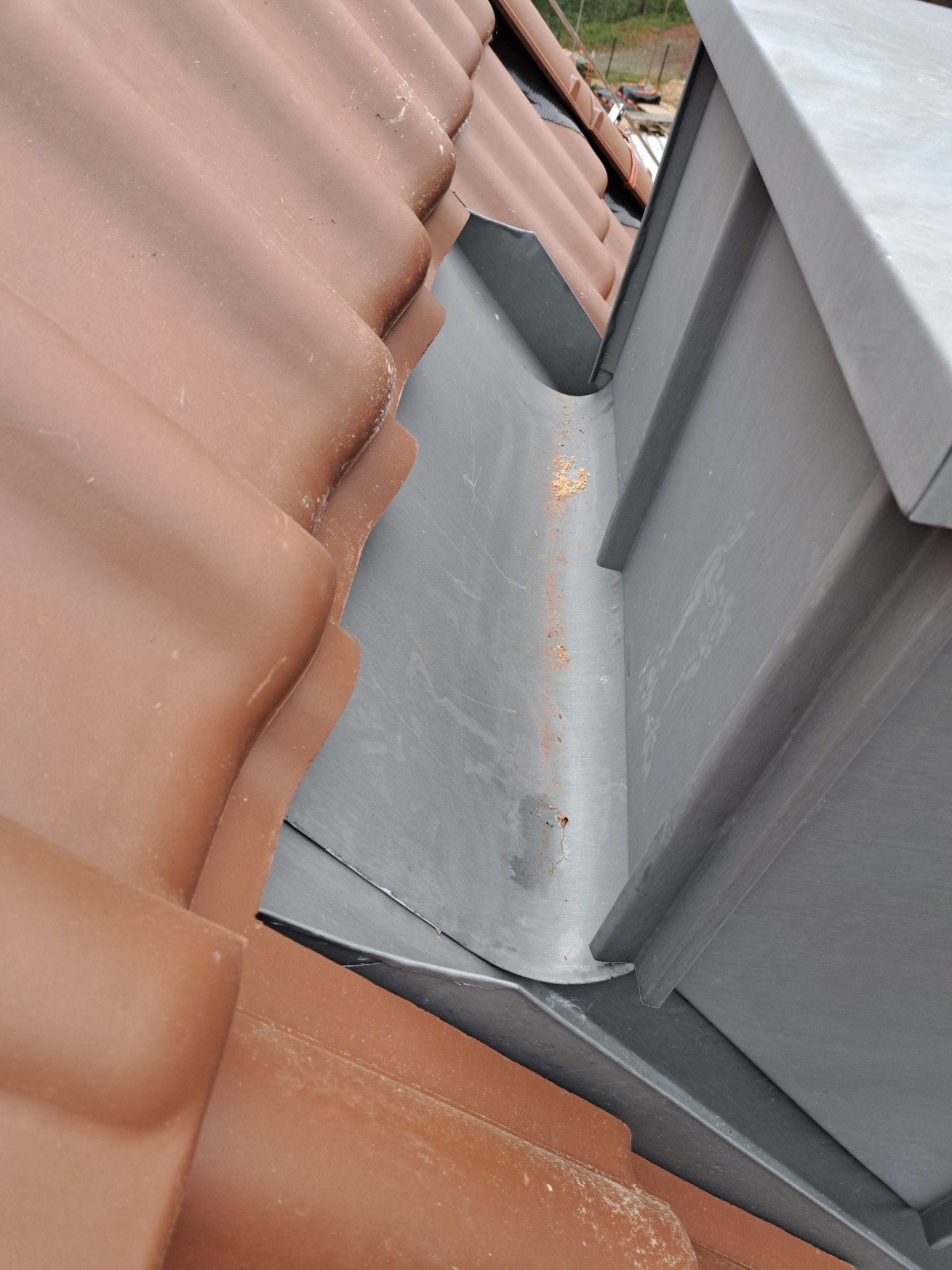 Nowa, szara rynna zamontowana przy brązowej dachówce ceramicznej. Widoczne detale łączenia elementów. Ujęcie z dołu, podkreślające precyzję wykonania.