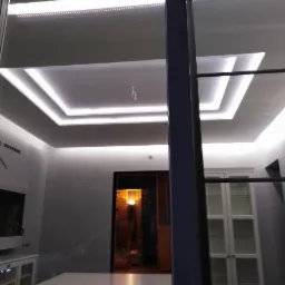 Nowoczesny sufit podwieszany z oświetleniem LED w kształcie kwadratów, widok z perspektywy przesuwanych szklanych drzwi, w tle widoczny salon z meblami.