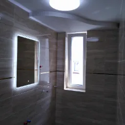 Wykończona łazienka z beżowymi płytkami imitującymi drewno, podświetlanym lustrem, białą ramą okienną i okrągłą lampą sufitową LED.