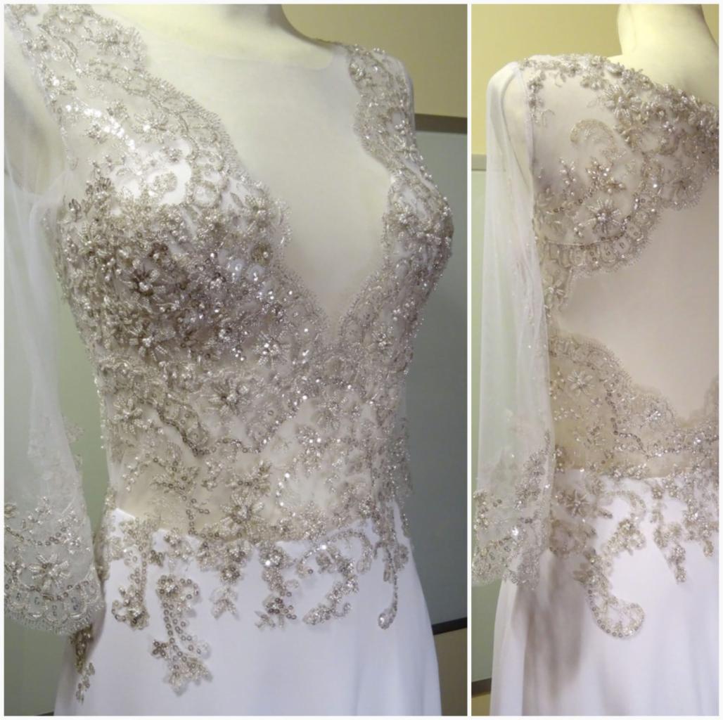Biała suknia z długimi, przezroczystymi rękawami, bogato zdobiona srebrnymi koralikami i cekinami w kwiatowe wzory, widoczna na manekinie.