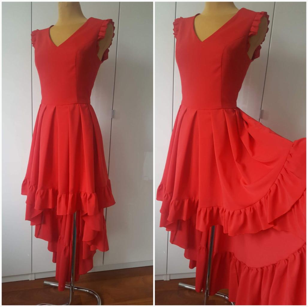 Czerwona sukienka z asymetrycznym dołem i falbanami, prezentowana na manekinie na tle białej szafy.