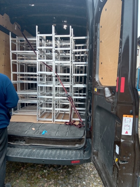 Wnętrze brązowego vana z otwartymi tylnymi drzwiami, wypełnione metalowymi regałami zabezpieczonymi pasami transportowymi.