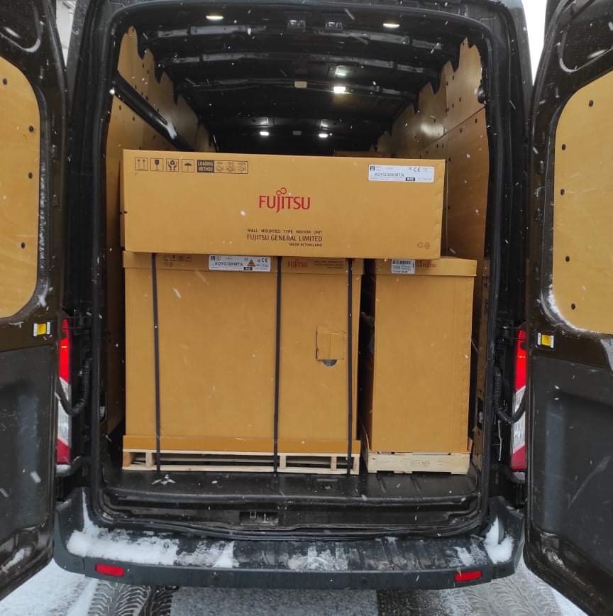 Wnętrze busa z otwartymi drzwiami załadowane kartonami marki Fujitsu na paletach, widoczne śnieżne otoczenie.