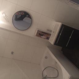 AdiDeccor - Nowa biała łazienka z umywalką z czarną szafką, okrągłym lustrem z odbiciem osoby robiącej zdjęcie, białą wanną i dozownikiem mydła w płynie.