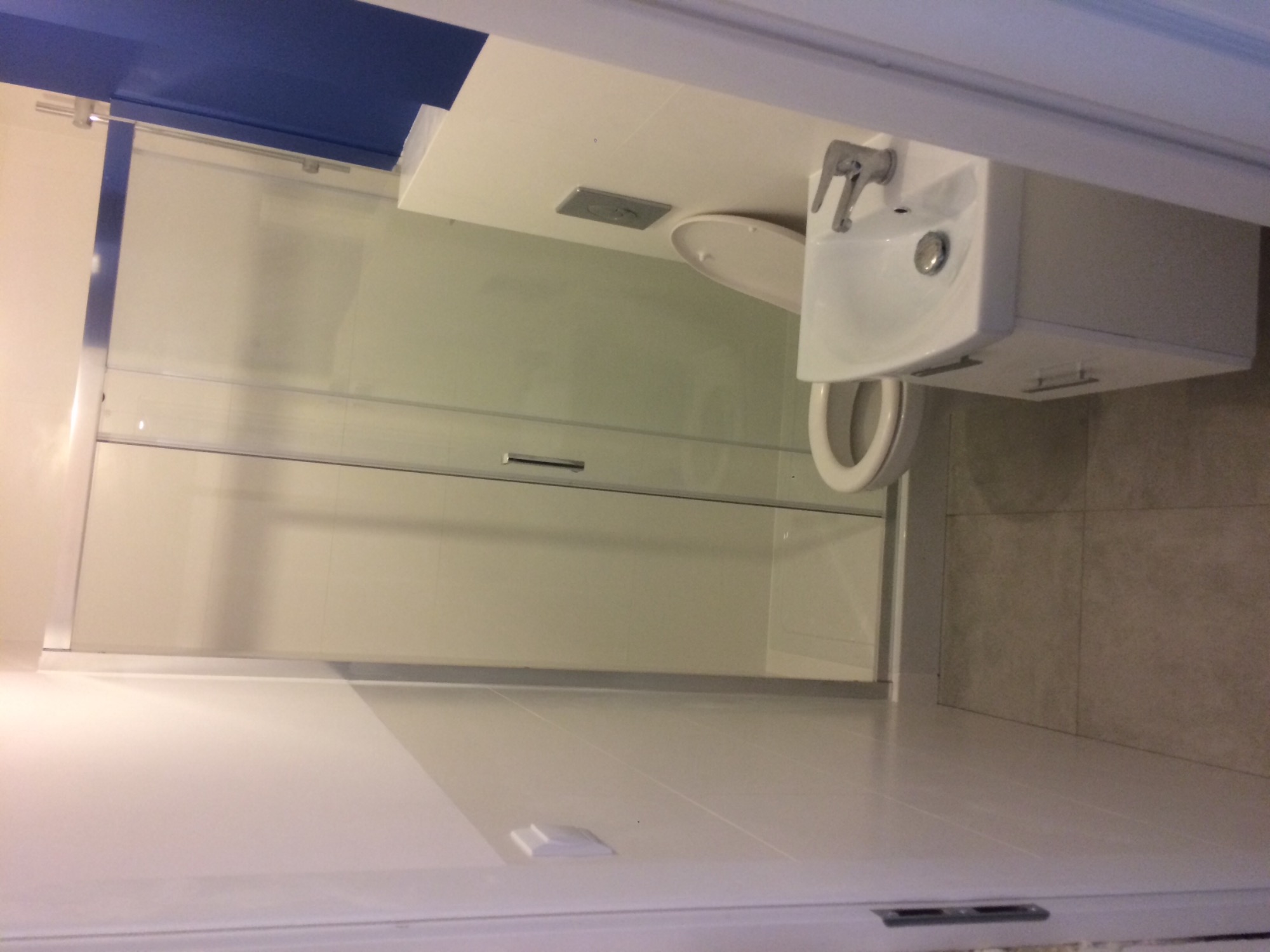 Nowoczesna łazienka z kabiną prysznicową ze szklanymi drzwiami, umywalką z szafką i toaletą w jasnych kolorach.