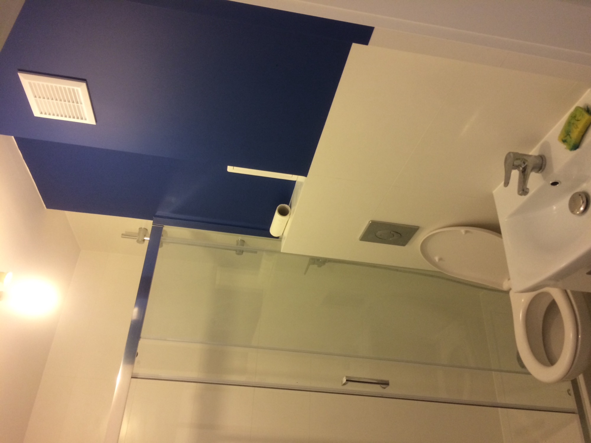 Wykończona łazienka z kabiną prysznicową, umywalką z baterią, toaletą i wentylacją pod sufitem pomalowanym na granatowo.