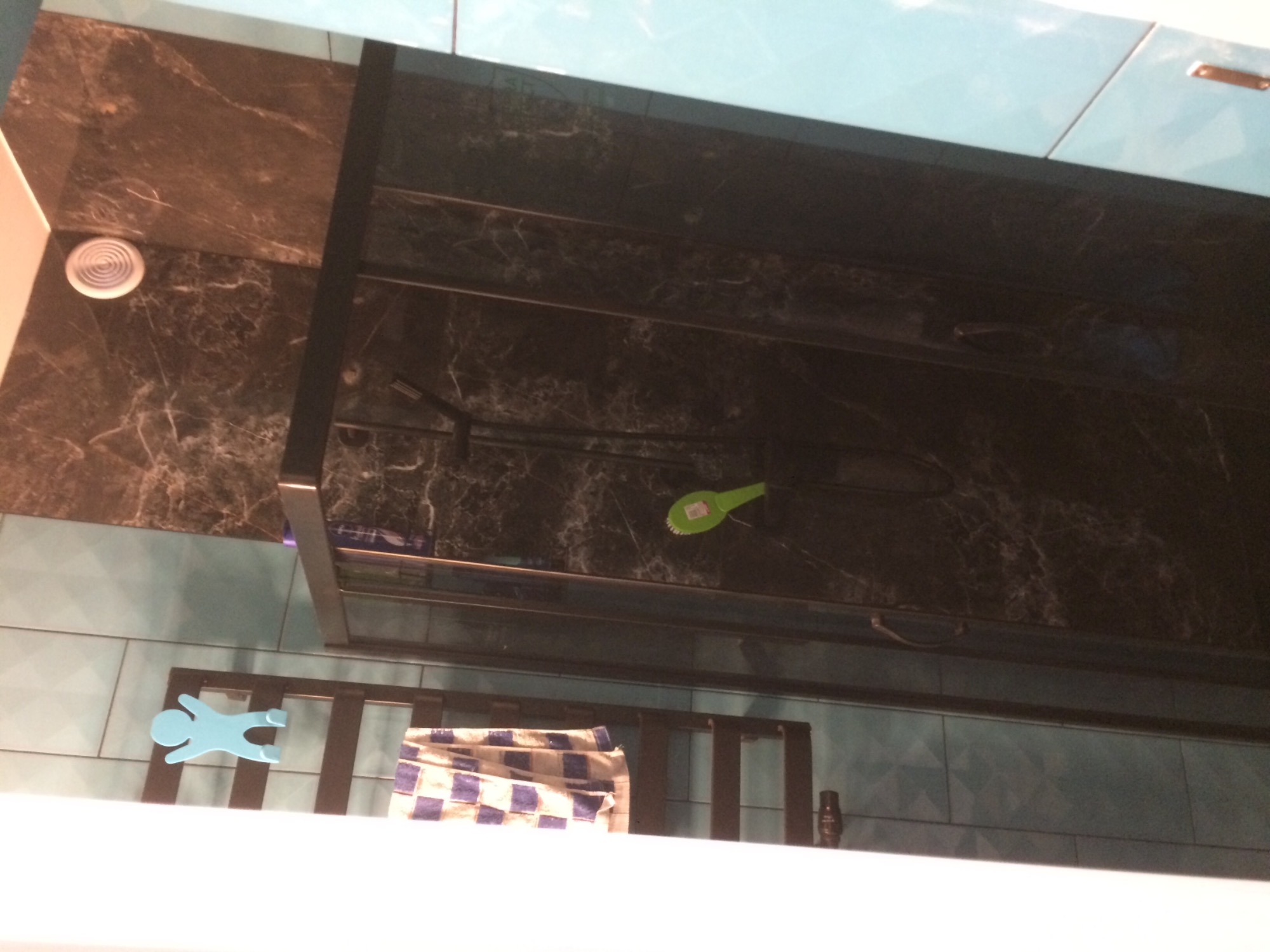 Szklana kabina prysznicowa z czarnymi profilami, zamontowana na ścianie wyłożonej błękitnymi płytkami, z widocznymi akcesoriami łazienkowymi i ręcznikiem w kratę.