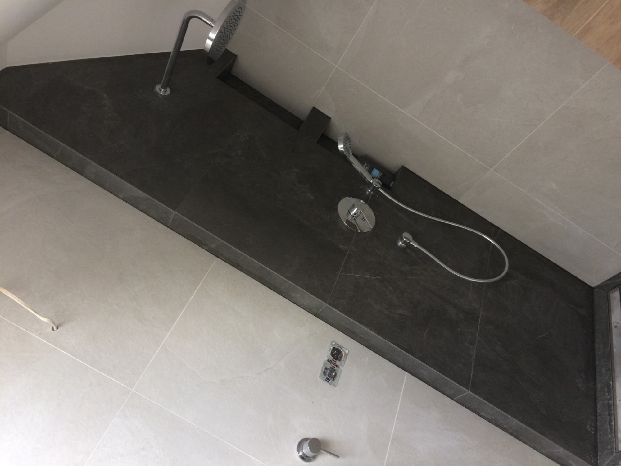 Wykończona kabina prysznicowa z szarą, kamienną ścianką, deszczownicą i baterią podtynkową, widoczne płytki w odcieniach szarości.