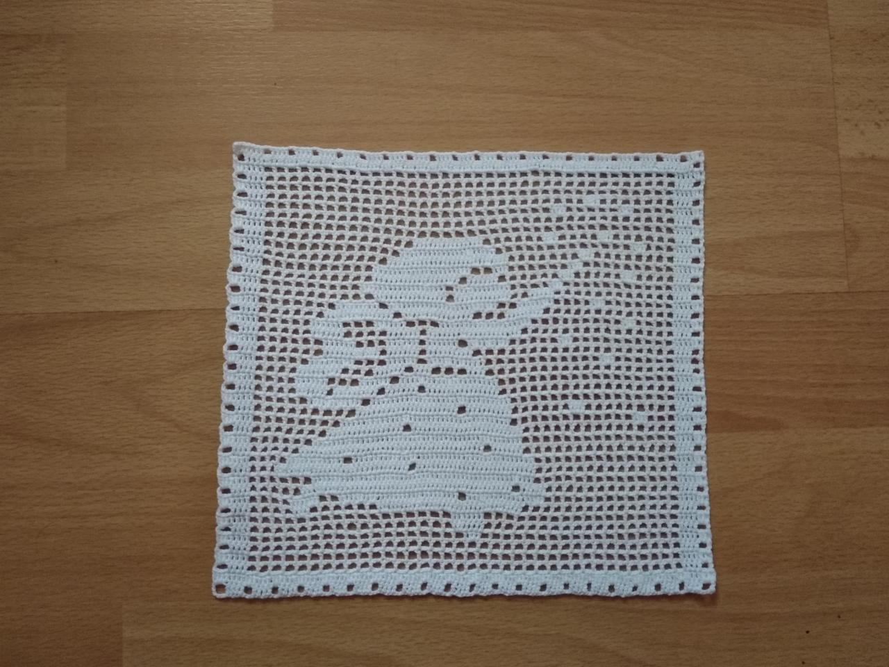 Biała, ręcznie robiona serwetka z ażurowym wzorem zajączka na drewnianym stole.