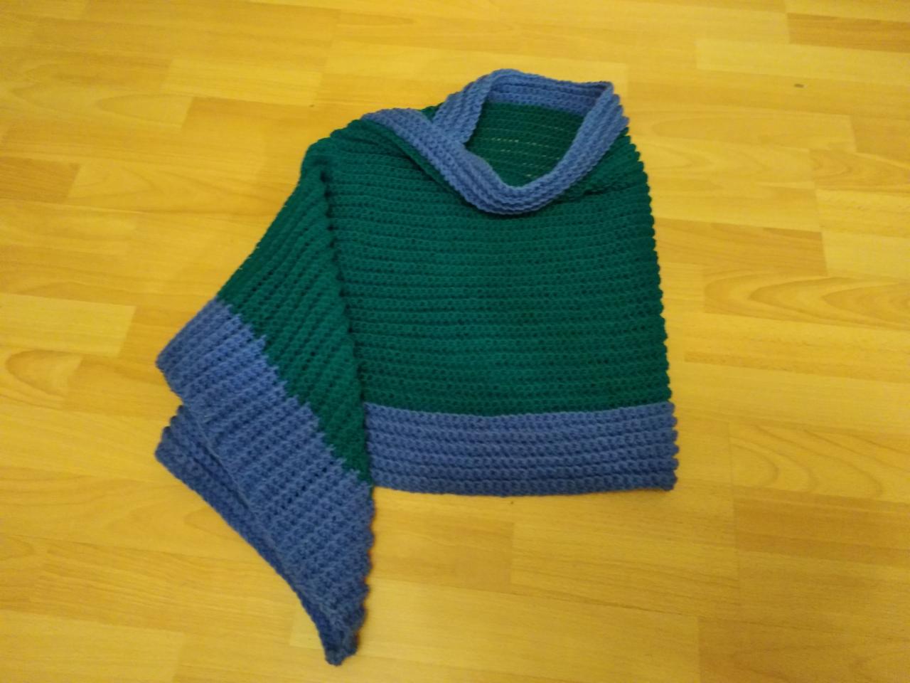 Zielono-niebieskie ponczo z dzianiny, ręcznie robione, leżące na drewnianej podłodze z widoczną fakturą splotu.