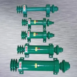 Zielone, metalowe wały z kołami pasowymi i mocowaniami, ułożone w rzędzie na metalowym tle, z naklejkami wskazującymi kierunek obrotu.