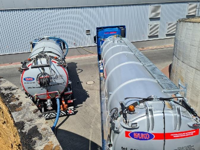 Dwa samochody ciężarowe z cysternami WUKO zaparkowane obok budynku przemysłowego, widok z góry, jeden z pojazdów ma podłączony wąż.