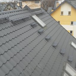 EKOMA SPORT - Szary dach z dachówki modułowej z zamontowanymi oknami dachowymi i elementami montażowymi. W tle budynek.