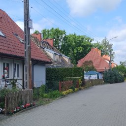 EKOMA SPORT - Ulica z domami w zabudowie szeregowej. Na jednym z domów widoczny remont dachu, odsłonięta konstrukcja i przygotowanie do położenia nowego pokrycia.