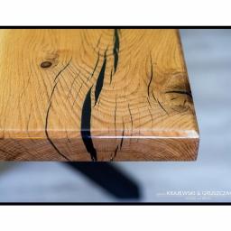 Krajewski & Gruszczak Wood and Resin - Fragment blatu z litego drewna dębowego z żywicą epoksydową w kolorze czarnym, wykończony na wysoki połysk, widoczny z boku, ukazujący słoje i naturalne pęknięcia wypełnione żywicą.