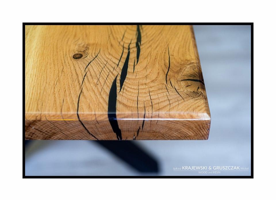 Fragment blatu z litego drewna dębowego z żywicą epoksydową w kolorze czarnym, wykończony na wysoki połysk, widoczny z boku, ukazujący słoje i naturalne pęknięcia wypełnione żywicą.