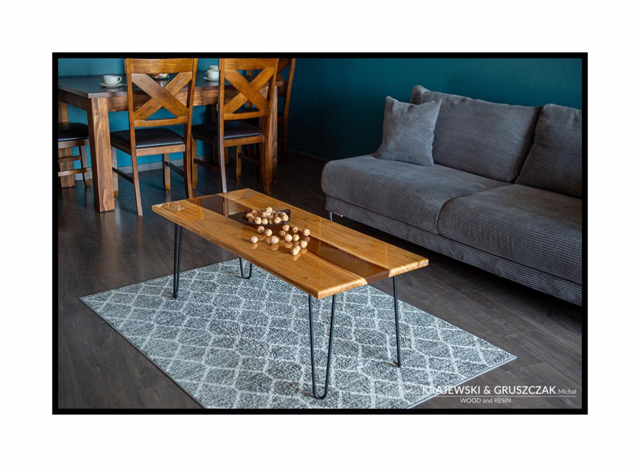 Stolik kawowy z drewna i żywicy epoksydowej na metalowych nogach, z orzechami w miseczce, na tle szarej sofy i dywanu w salonie w Krakowie.