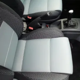 Wnętrze samochodu z odnowioną tapicerką foteli w kolorze szarym z czarno-białą kratką, widoczna dźwignia zmiany biegów i hamulec ręczny.