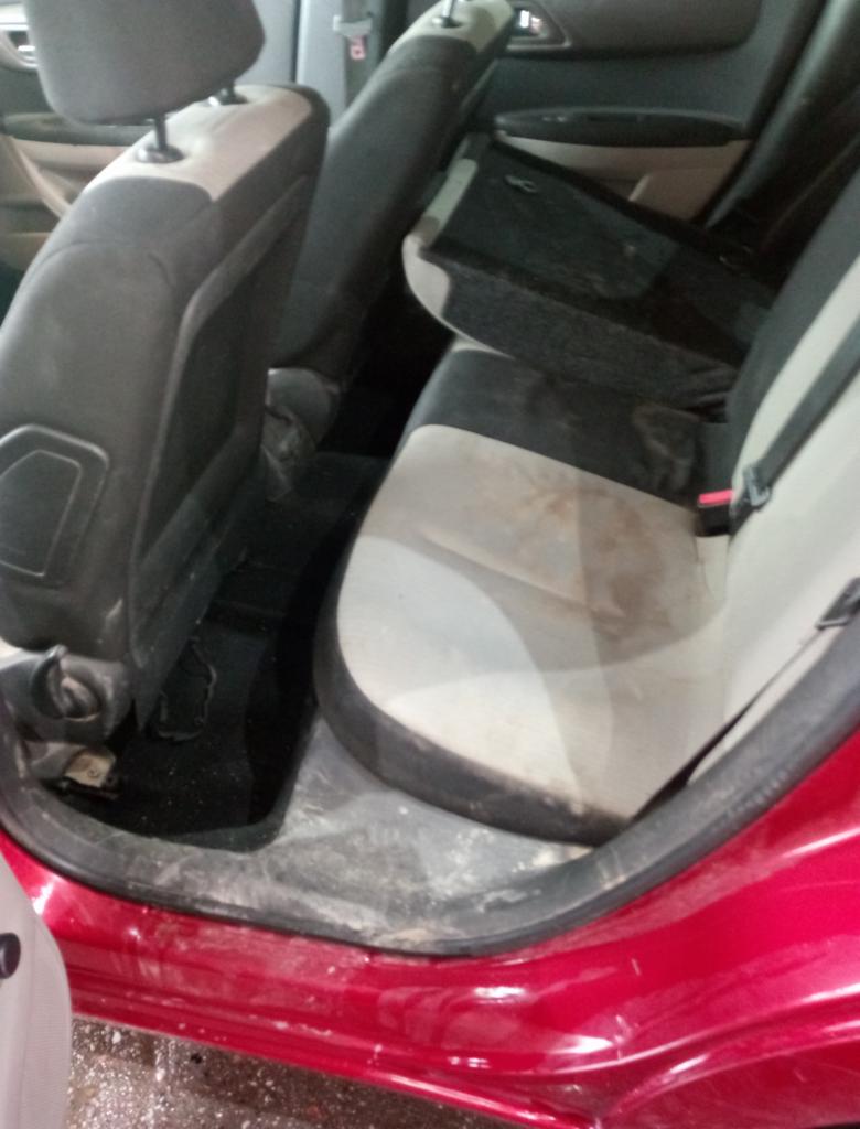 Wnętrze czerwonego samochodu z widocznymi, zabrudzonymi tylnymi siedzeniami z szarej tapicerki. Widoczne plamy i zanieczyszczenia na siedzeniach oraz podłodze pojazdu.