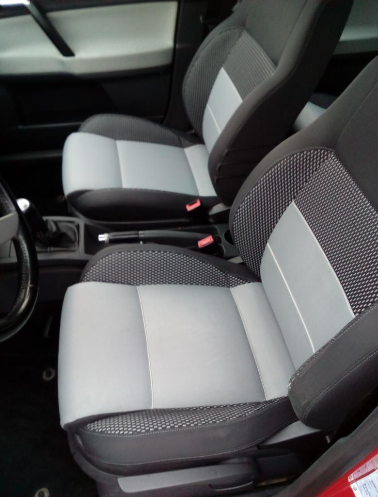 Wnętrze samochodu z dwoma przednimi fotelami po renowacji tapicerki w odcieniach szarości i czerni, widoczne detale wykończenia i faktura materiału.