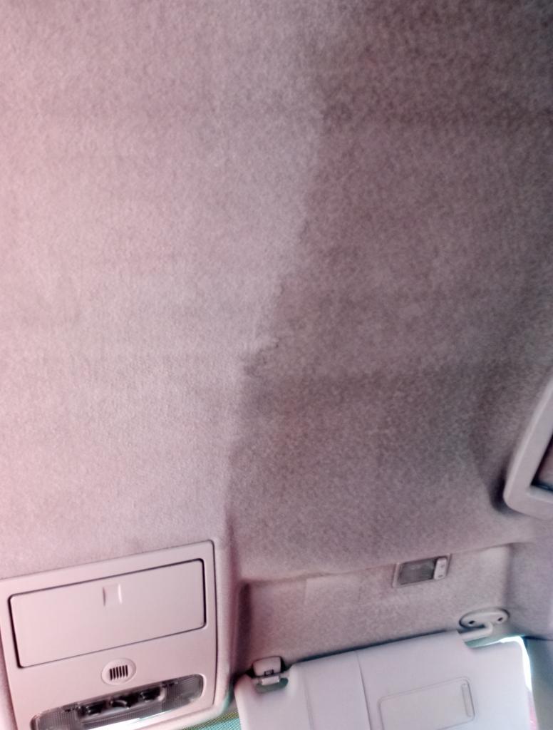 Wnętrze samochodu: widoczny fragment podsufitki z wyraźną różnicą w czystości po czyszczeniu, lewa strona jaśniejsza i czysta, prawa strona ciemniejsza i zabrudzona, widoczne elementy oświetlenia...