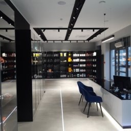 Refresh - Nowoczesne wnętrze sklepu z suplementami diety, z minimalistycznym oświetleniem, szarymi podłogami z wbudowanymi liniami LED, czarnymi regałami wypełnionymi produktami i niebieskimi krzesłami...