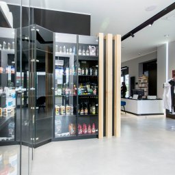 Refresh - Wnętrze sklepu z kosmetykami samochodowymi: szklane gabloty z produktami na półkach, jasna podłoga, minimalistyczny wystrój, widoczna ekspozycja ubrań z logo marki.