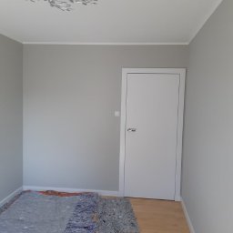 Refresh - Pokój po malowaniu ścian na szaro, widoczna biała stolarka drzwiowa i zabezpieczona podłoga, ozdobna lampa sufitowa.